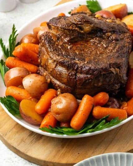 A pot roast served with carrots and potatoes on a serving platter.