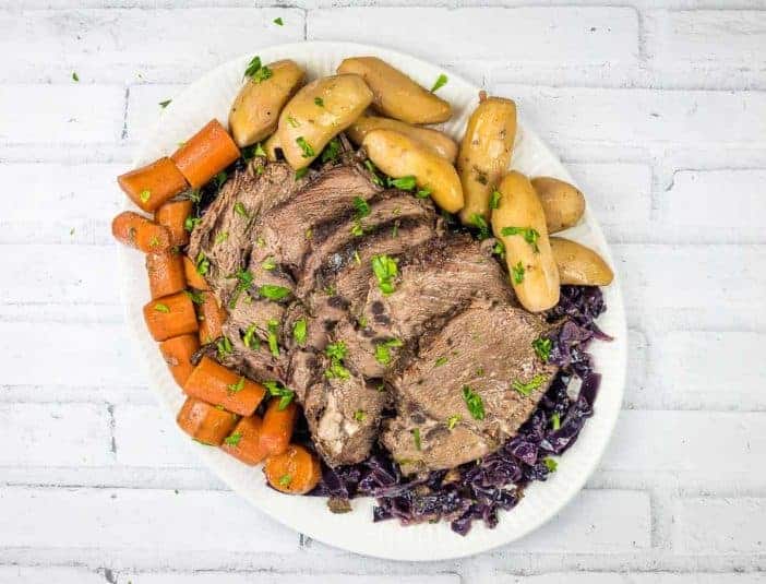 A plate of German pot roast beef with a sauce being poured over it.