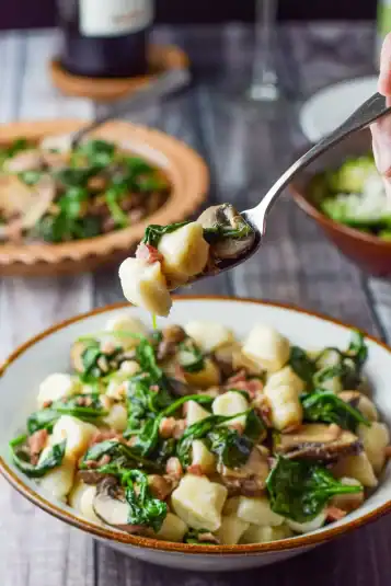 A fork with the gnocchi on it held over the bowl with more veggies in the background.