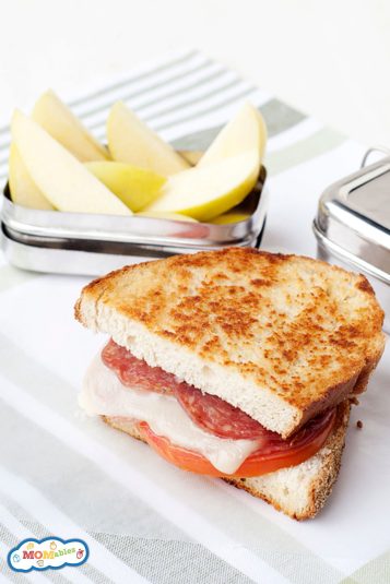 Grilled pepperoni sandwich with melted cheese and tomato next to sliced pears.