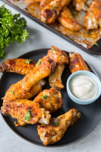 Keto Chicken Wings on a black plate with parsley and a white sauce.