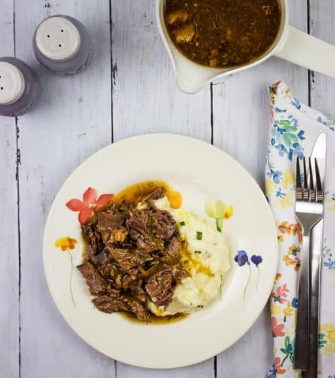 A plate of pot roast with bacon and mashed potatoes with gravy.