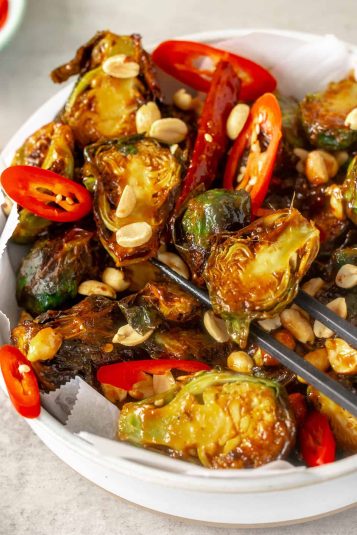 Kung pao brussel sprouts in a serving dish, with chopsticks lifting a sprout.