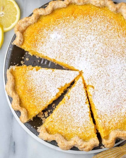 A sliced lemon chess pie sitting on a white marble table.