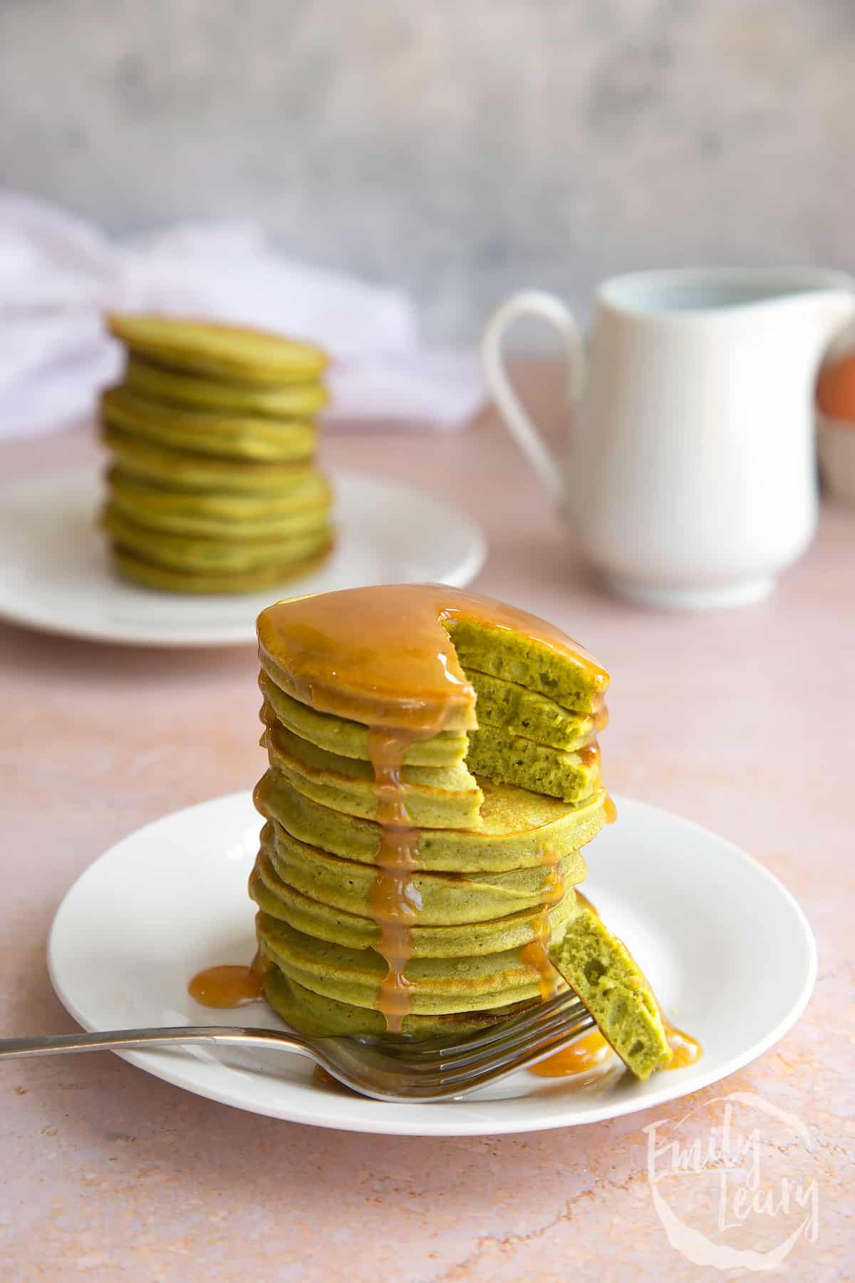 A stack of matcha pancakes on a white plate and fork with a section cut out.