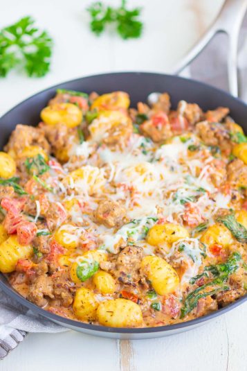 A skillet of Italian sausage gnocchi, topped with shredded mozzarella cheese.