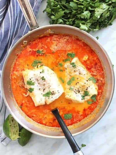 Overhead shot of poached fish in a skillet with fresh cilantro garnish.