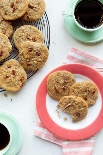 Pink rimmed plate of praline cookies along with cooling rack and mint green cups of coffee.