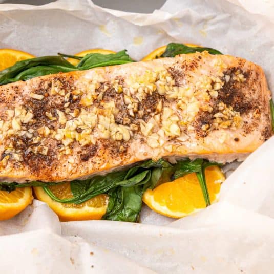 Salmon al cartoccio in a crinkled parchment cradle on a bed of spinach and orange slices.