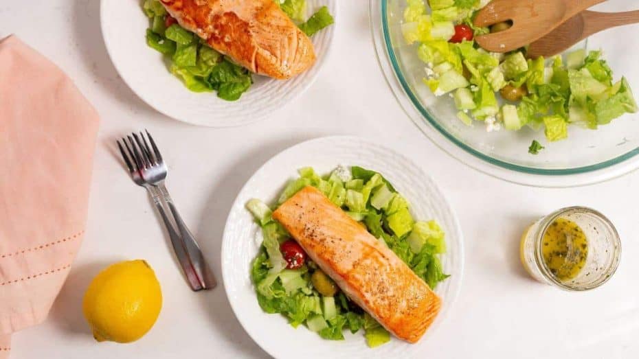 Salmon salad on white plates and lettuce greens in a bowl.