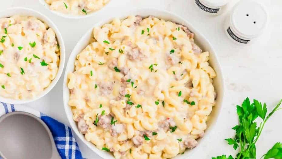 A bowl of macaroni and cheese with sausage and parsley.