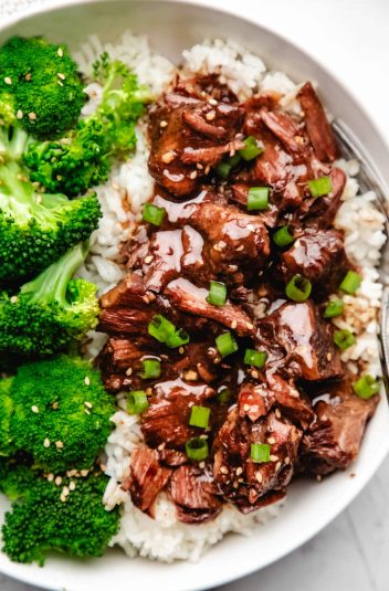 Close up photo of slow cooker Korean beef over white rice next to steamed broccoli.