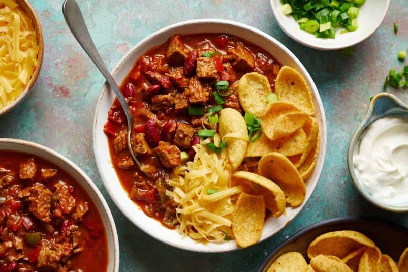 Three bowls of chili filled with toppings, featuring beans and meaty steak.