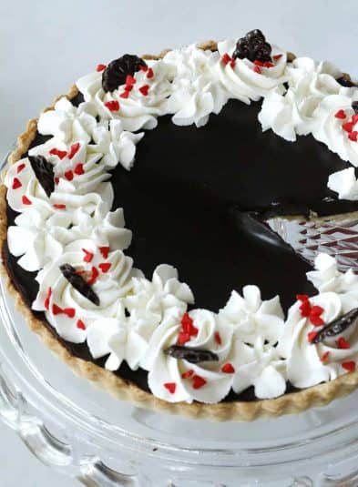 A slice of a chocolate tart with whipped cream on top on a white plate.