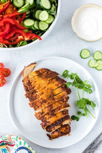 Mexican Chicken Breast on a white plate with a bowl of salad.
