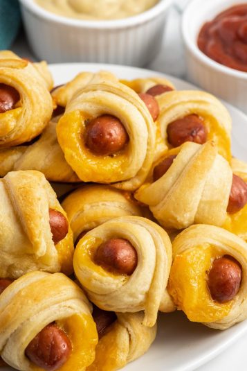 Pigs in a blanket stacked on a white plate.
