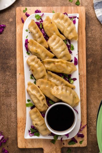 A white rectangular plate of ground turkey potstickers served with a small bowl of soy sauce on a wooden board, garnished with chopped purple cabbage and cilantro.