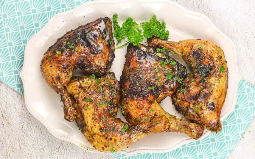A white platter with four seasoned and cooked chicken quarters, garnished with fresh parsley.
