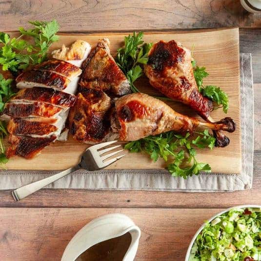 A carved grilled turkey on a wooden board with gravy and salad nearby.