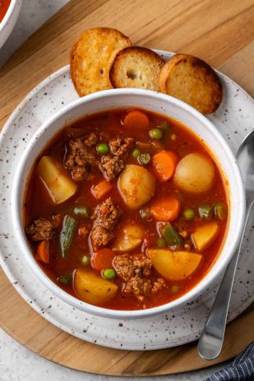 A bowl of hamburger soup served alongside garlic toast.