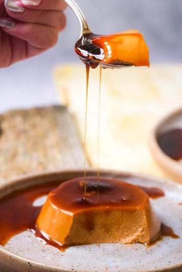 A spoon lifts a piece of Pumpkin flan from a plate, with caramel sauce drizzling down.