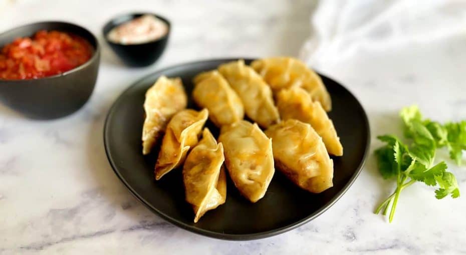 Taco dumplings on a plate with salsa and sour cream on the side.