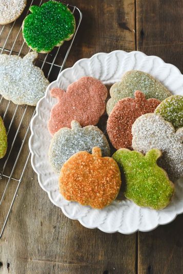 Colorful sugar sprinkled pumpkin sugar cookies on a plate.