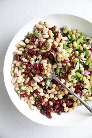 Large white bowl filled with vegetarian three bean salad made with red kidney beans, cannellini beans, and garbanzo beans.