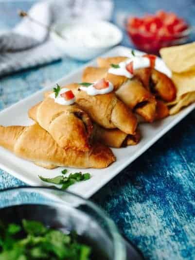 Crescent taco rolls on a platter with sour cream and tomatoes.