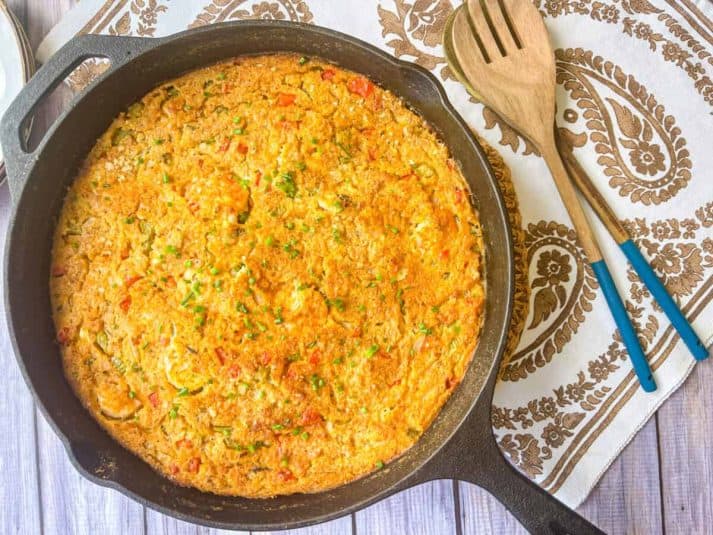 Finished recipe baked in a cast iron skillet next to wooden serving spoons.
