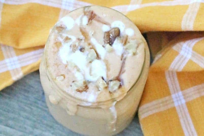 Glass with cookies and cream shake topped with coconut whipped cream and crumbled cookies with a striped straw in it. There are straws, chocolate chip, cookies and chocolate chips around the glass.