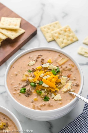 A bowl of cheeseburger soup with a spoon and crackers.