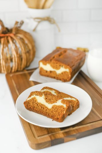 Sliced pumpkin cream cheese bread on a white plate with a full loaf behind it.