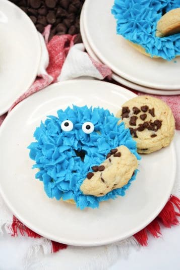 White plate with donut topped with blue frosting with edible eyes and cookie.