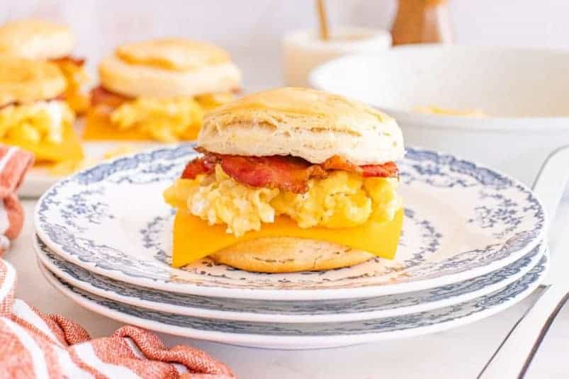 Biscuit breakfast sandwiches with scrambled eggs, cheddar cheese, and bacon are served on a blue-patterned plate.