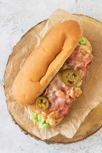 A Mexican breakfast torta sitting on a wooden cutting board and showing the filling.