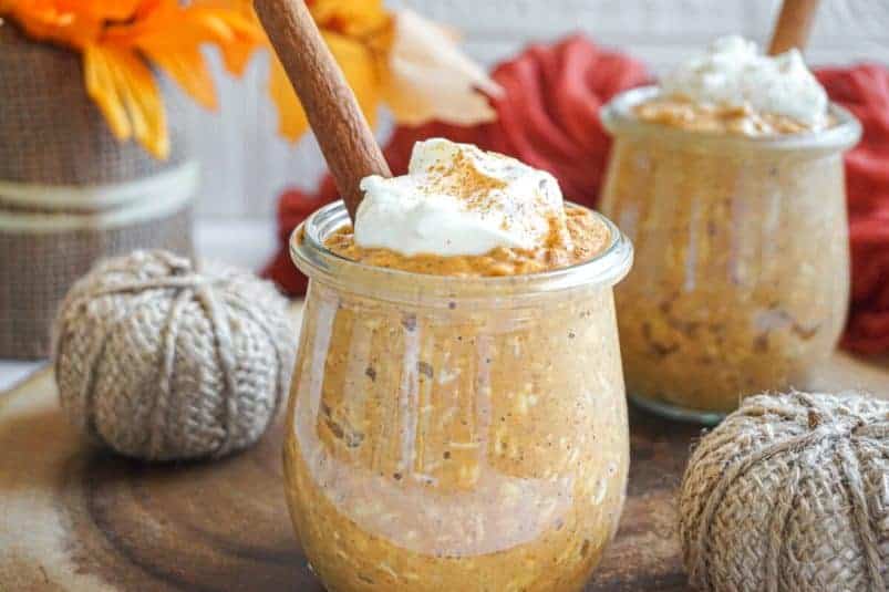 Front view of pumpkin pie overnight oats topped with Greek yogurt and dusted with cinnamon. Pumpkins and leaves in the background.
