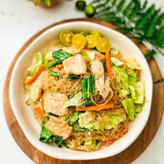 Plate of Pancit with Chicken, garnished with assorted toppings like lemon wedges, green onions, and crispy fried garlic, offering a vibrant and flavorful presentation.