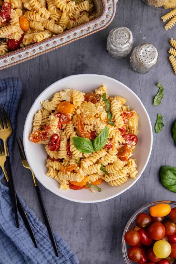 Feta Pasta Recipe plated and garnished with fresh basil beside casserole dish and fresh tomatoes.