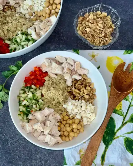 A fully assembled Mediterranean grain bowl on a counter, next to a decorative towel with a wooden spoon.