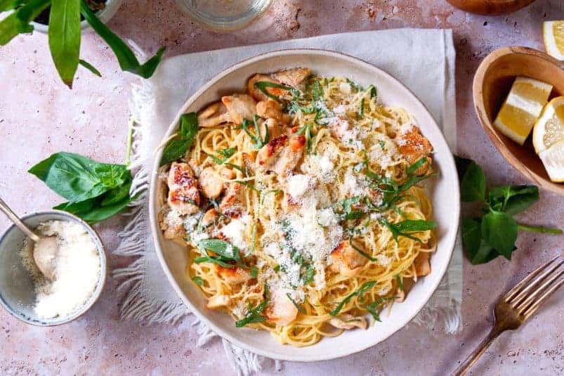 Lemon basil pasta on white plate with lemons, grated Parmesan and fresh basil on the side.