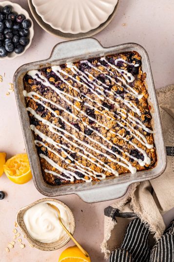 Lemon blueberry baked oatmeal in a baking dish, topped with a lemon yogurt drizzle.