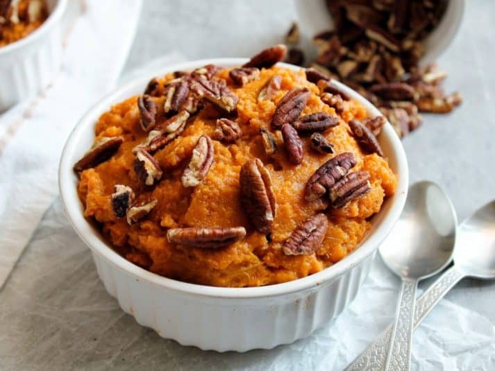 Mashed sweet potatoes in a white serving bowl, topped with toasted chopped walnuts.
