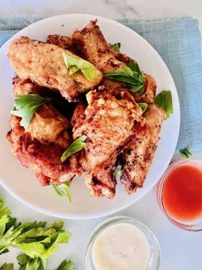 Naked Chicken Wings Piled on a plate with minced parsley next to dips in small bowls.