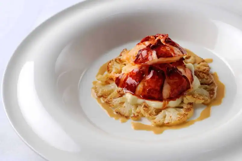 Poached Lobster Tail w/ Cauliflower and Lobster Butter Sauce on a white plate.