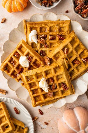 Golden brown pumpkin pecan waffles on a plate with whipped cream and cinnamon.