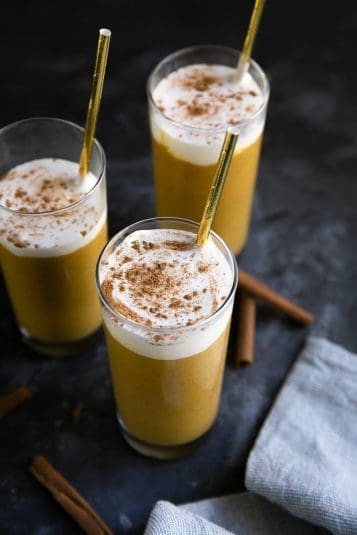 Three glasses filled with pumpkin smoothie and topped with whipped cream and sprinkled with cinnamon.