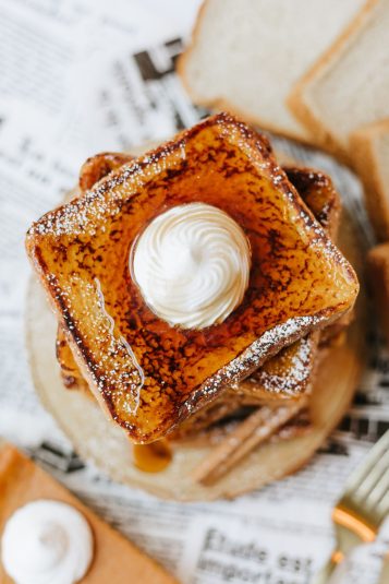 Overhead shot of a stack of pumpkin french toast topped with whipped cream, maple syrup, and powdered sugar.