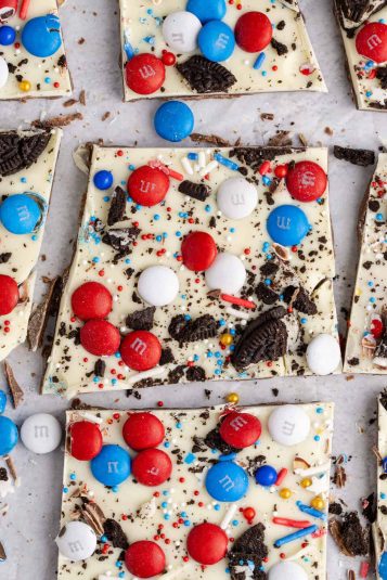 Red White and Blue Candy Bark with M&Ms Oreos and sprinkles cut up on parchment paper.