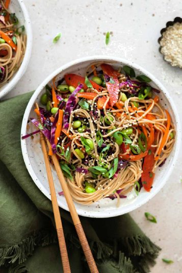 Overhead view of soba noodle salad in a white bowl with chopsticks on the side.